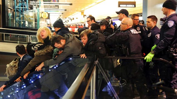 Seattle police push the last group of protesters down stairs and out of a Seattle-Tacoma International Airport terminal.