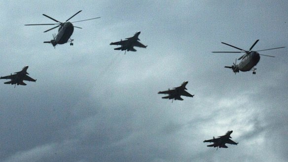 Military helicopters and fighter jets rehearse overhead.