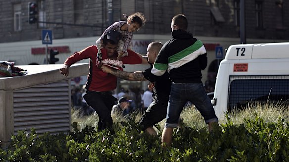 A Syrian man carrying a child scuffles with a Hungarian nationalist in front of Keleti train station in Budapest.