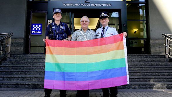 Transgender police officer Constable Mairead Devlin with Brisbane LGBTIQ Action Group convener Phil Brown and QPS LBGTIQ Support Network convener Sergeant Mick Gardiner stand proud with the rainbow flag outside the Brisbane police headquarters on Roma Street.