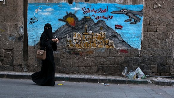 A woman passes a mural depicting airstrikes in Sanaa, Yemen.