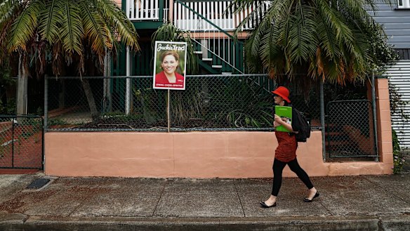Greens candidate for South Brisbane Amy MacMahon walks past a corflute of Deputy Queensland Premier Jackie Trad.