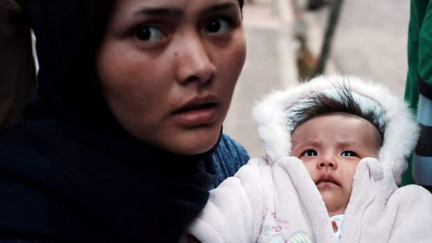 An Afghan woman holds her child as she boards a bus taking migrants from an Athens park to a centre for the displaced.