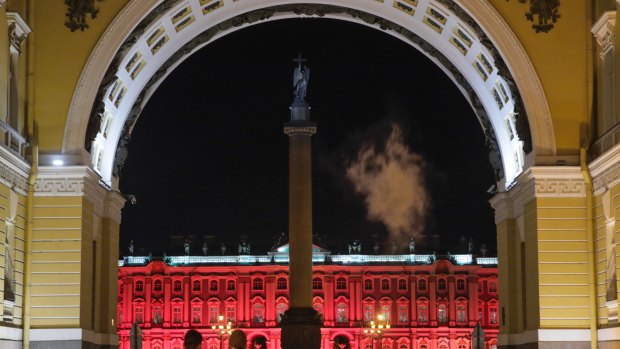 People walk past the Winter Palace in St Petersburg, illuminated in red for the upcoming 100th anniversary of the Bolshevik revolution.