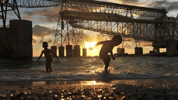 Children play beneath the hulking cantilevers used to load phosphate on ships.