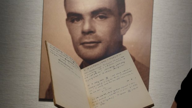A notebook of British mathematician and pioneer in computer science Alan Turing in front of a photo of him during an auction preview.