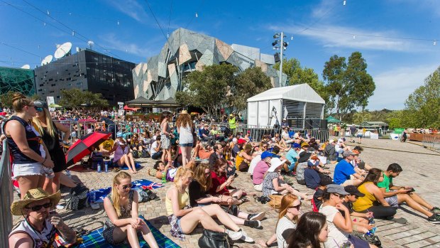 Fans settle in at Federation Square to watch the grand final in the sun.