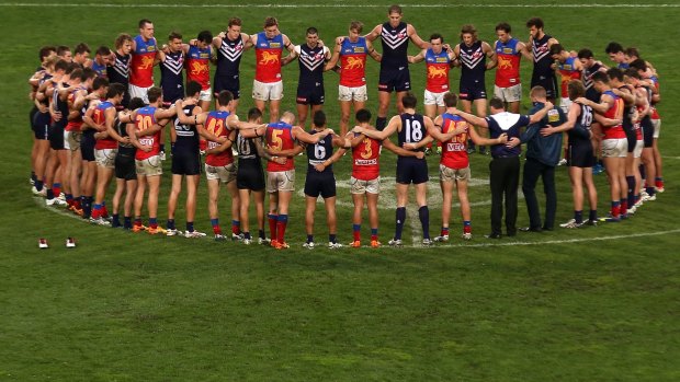 Players and coaches from Fremantle and Brisbane stand in silence around the centre circle as a mark of respect to former Crows coach Phil Walsh.