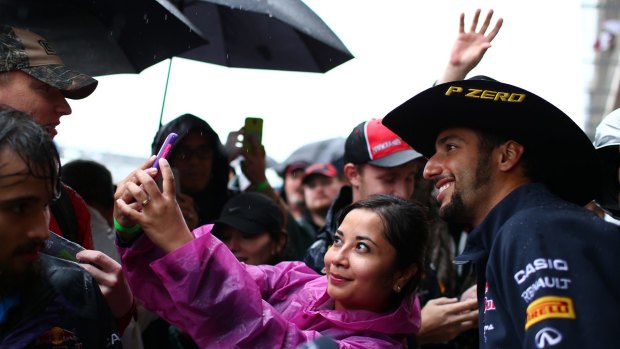 Daniel Ricciardo poses for photographs with fans in pit lane.