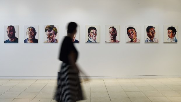 A woman walks past a series of paintings of the Bali Nine by Myuran Sukumaran that are a part of the <I>Another Day in Paradise</I> exhibition.