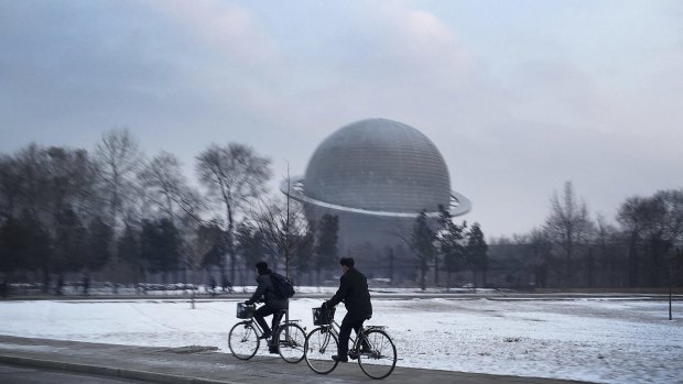North Koreans cycle past a planetarium at the Three Revolutions Exhibition Hall.