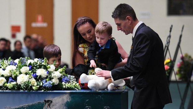 Senior Constable Brett Forte's children Sam, Emma and Brodie place a teddy bear and other items on his casket during his funeral service in Toowoomba.