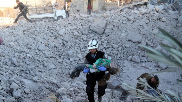 A man carries a wounded child over the wreckage of collapsed buildings after Russian forces carried out air strikes on residential areas in Yaqid al-Adas, near Aleppo.