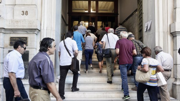 A National Bank official opens the door of a bank branch as people enter after Greek banks reopened on Monday morning.