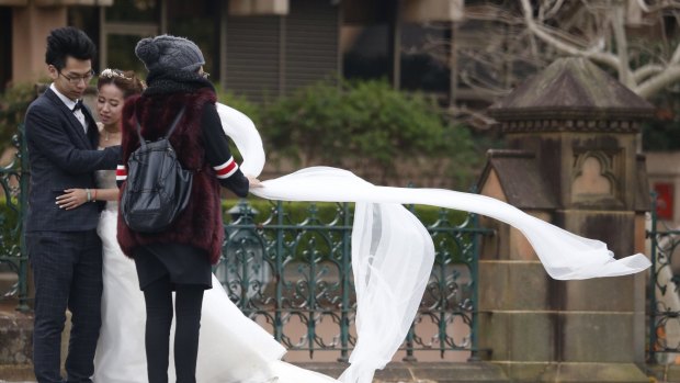 A bride and groom shelter from the gusts of wind outside St Mary's Cathedral, as Sydney's weather reverts to winter.