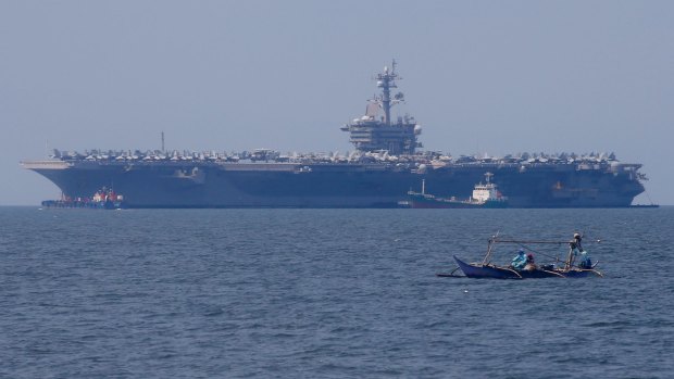 Fishermen on board a small boat pass by the USS Carl Vinson aircraft carrier.