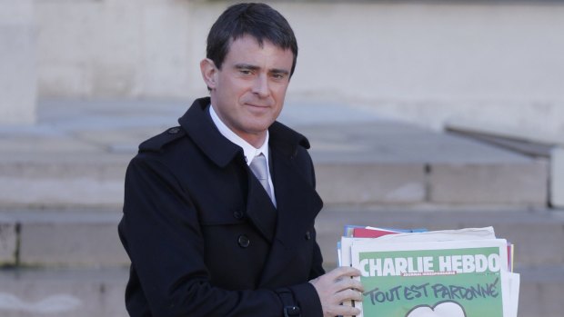 French Prime Minister Manuel Valls holds a copy of <i>Charlie Hebdo</i> with the title "Tout est pardonne" ("All is forgiven") as he leaves the weekly cabinet meeting at the Elysee Palace in Paris.