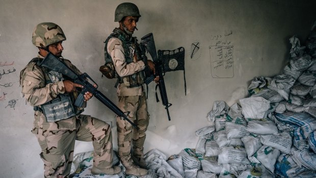 Iraqi army soldiers stand by an Islamic State flag drawn on a wall in a house damaged by a US airstrike on the town of Kabrouk in May.