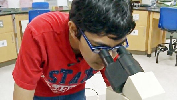 Tanishq Abraham looks into a microscope in a lab at American River College in Sacramento.