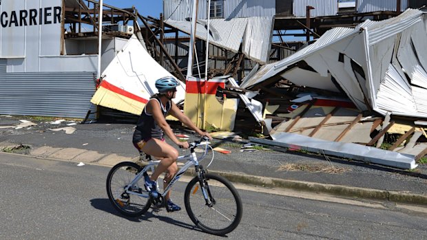 A resident rides past a cyclone damaged business in Rockhampton.