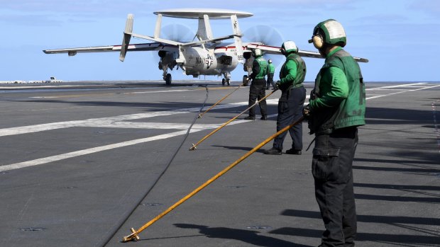 Personnel prepare to manoeuvre the arresting cable released from a E-2 Hawkeye communication aircraft after landing on board .