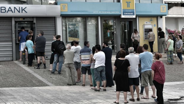 People stand in a queue to use ATM machines to withdraw cash at a bank in Athens.