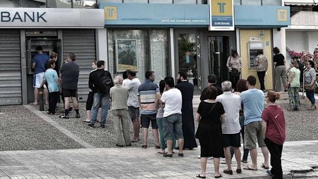 People stand in a queue to use ATM machines to withdraw cash at a bank in Athens.