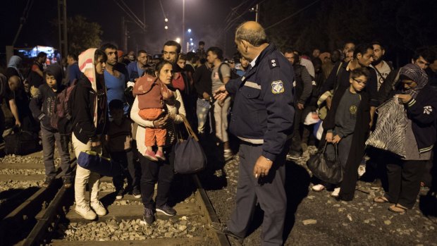 A Greek police officer gives orders to Syrians as they wait to cross the border from Greece to Macedonia at the weekend. 