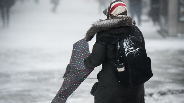 A pedestrian battles with an umbrella in strong winds in New York City. Fast-moving winter storm have grounded 3000 flights and closed schools.