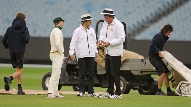 Tasmanian captain George Bailey speaks with umpires Geoff Davidson and Geoff Joshua as the groundsmen put the covers on at the MCG on Wednesday.