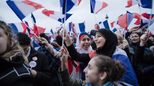 Supporters of Emmanuel Macron wave French flags while reacting as vote projections are announced in the second round of the French presidential election in Paris.