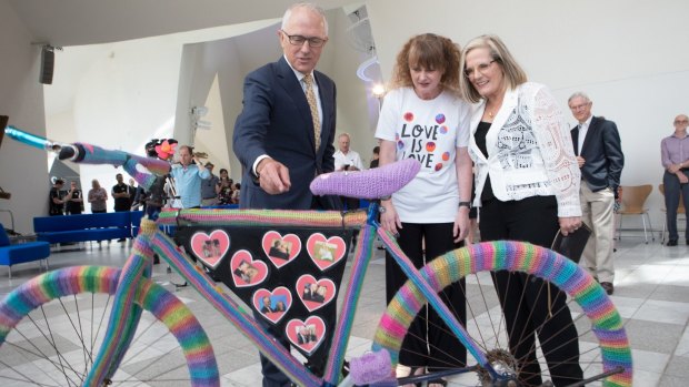 Prime Minister Malcolm Turnbull with the crocheted Love Wheels bike, its artist Eloise Murphy and his wife Lucy at the National Museum of Australia on Thursday. The bike is adorned with pictures of the Turnbulls, celebrating their almost 38-year marriage, as well as the successful YES campaign in the marriage equality vote.