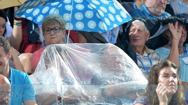Tennis fans take shelter from the rain at Pat Rafter Arena on Monday.