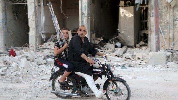 A man with a leg cast rides a motorcycle though a bomb-damaged area in Old Aleppo on Thursday.