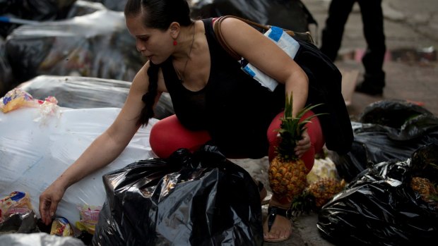 A pregnant woman who did not want to be named holds a pineapple in one hand as she continues to pick through garbage bags outside a supermarket in downtown Caracas.