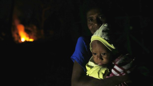 A woman holds her three-year-old outside their damaged home as night falls in Tanna.