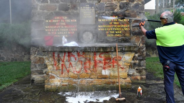 Council workers clean anti-war graffiti which was sprayed on the Warrandyte war memorial.