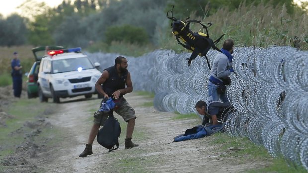 Hungarian police watch as Syrian migrants climb under the fence near Roszke.