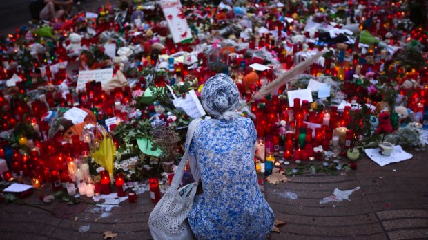 A woman sits next to candles and flowers placed on the ground after a terror attack that killed 14 people in Barcelona.