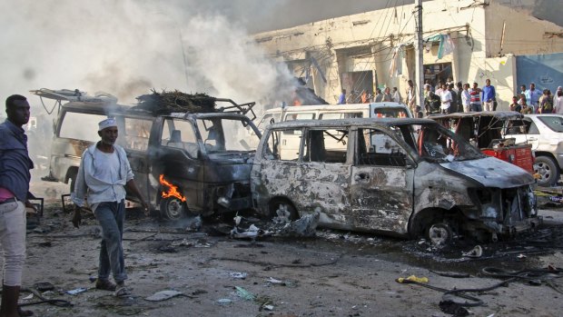 Somalis walk past the wreckage of vehicles at the scene of a blast in Mogadishu.
