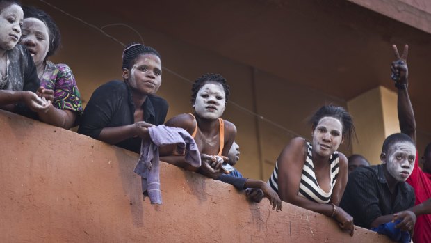 Residents on a balcony wear a white substance on their faces on Monday to protect against tear gas as they watch riot police chase angry supporters of opposition leader Kizza Besigye.