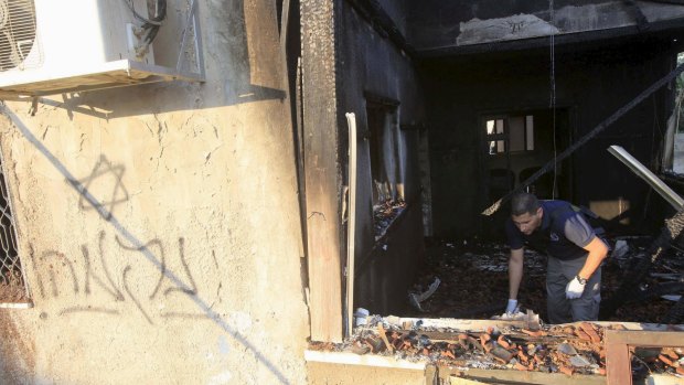 An Israeli police officer inspects the charred remains of the Dawabshes' home, with graffiti, reading "revenge", clearly visible.