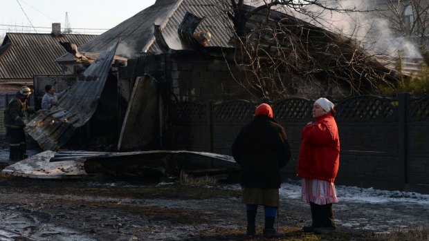 Residents look on as firemen try to extinguish a fire after a shell hit a home in Donetsk.