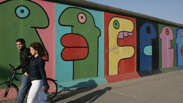 A young couple walk past the East Side Gallery in Berlin.