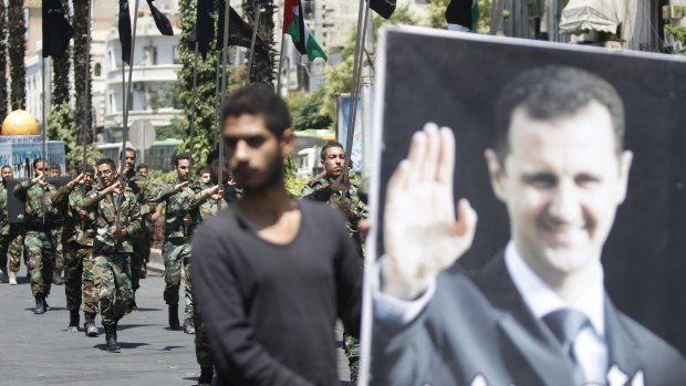 Regime loyalists carry flags as one of them holds a picture depicting Syrian President Bashar al-Assad during a rally marking Jerusalem Day in Damascus on July 10.