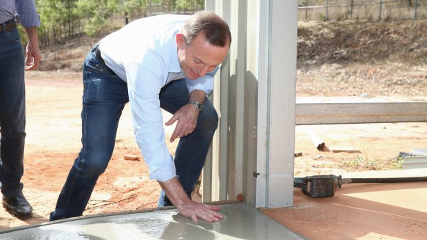 Prime Minister Tony Abbott makes a handprint in the wet cement as he assists in the community hall upgrade in the Injinoo community, during his visit to Cape York.