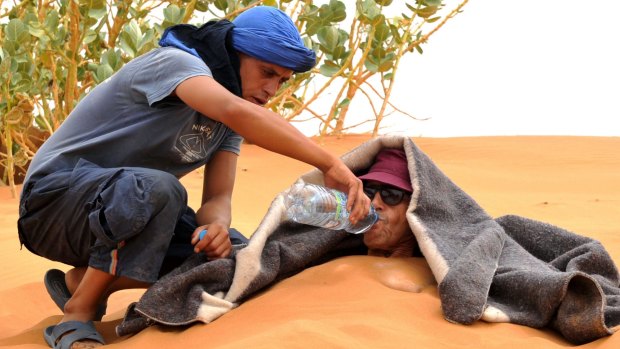 A tourist is served water as he takes a sand bath in the dunes of the Merzouga desert.