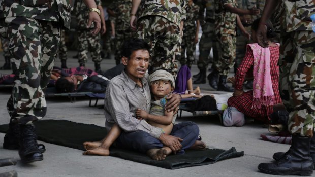A man sits with a child on his lap as victims of Saturday's earthquake wait for ambulances after being evacuated to Kathmandu, Nepal.