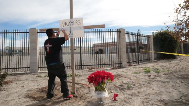 Manny Guzman erects a cross and a sign outside the police perimeter around the Inland Regional Centre, the site of a mass shooting on Wednesday that left 14 dead and 21 wounded, in San Bernardino, California.