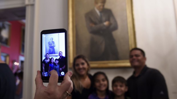A family takes a photo in front of a portrait of President John F. Kennedy hanging in the Cross Hall during a tour of the White House in Washington.